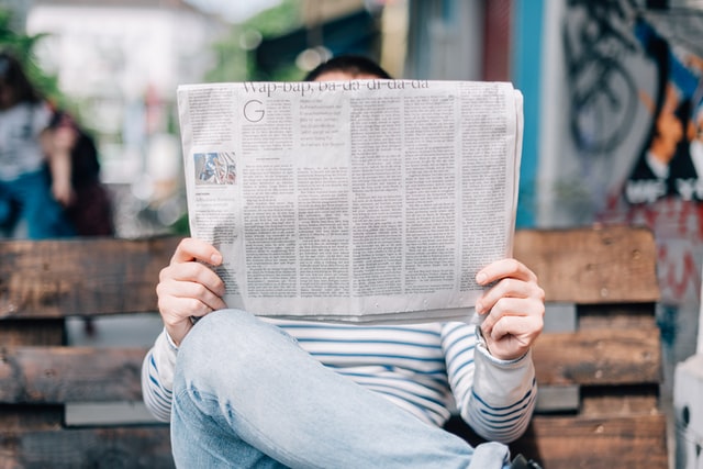 Person holding newspaper in front of their face to read