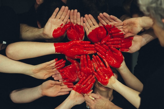 Many hands joined together palms up, with a heart painted across them.